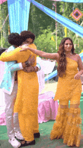 a woman in a yellow dress is hugging two men in blue jackets