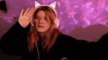a woman wearing headphones and a cat ear headband is dancing in front of a purple background .