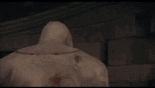 a statue of a man with a hood is standing in front of a brick wall .