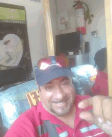 a man wearing a red shirt and a black hat is smiling and pointing