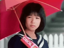 a young girl is holding a red umbrella and a candy bar with the word cecil on it .