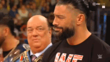 a man with a beard is standing next to another man in a black shirt with the word wwe on it .