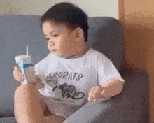 a little boy is sitting on a couch holding a carton of milk and a straw .