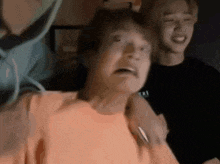 a man in an orange shirt is making a funny face while standing next to another man .