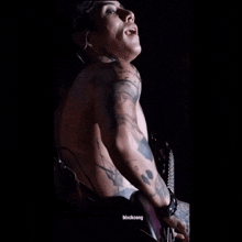a shirtless man with tattoos on his arms and chest is playing a guitar in a dark room
