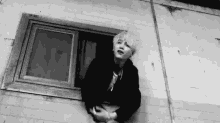 a black and white photo of a person leaning out of a window of a building .
