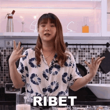 a woman in a floral shirt is standing in front of a kitchen counter with the word ribet written on it