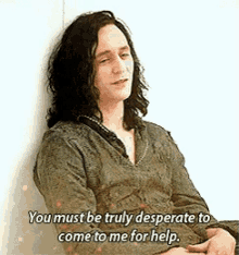 a man with long hair is leaning against a wall and talking to someone .