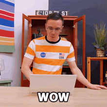 a man in an orange and white striped shirt is using a laptop and the word wow is on the desk