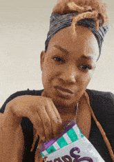 a woman with dreadlocks is eating a bag of candy that says ' snickers ' on it