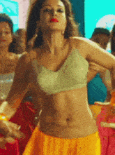 a woman in a green crop top and yellow skirt is dancing in front of a crowd .
