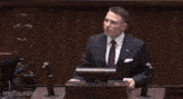 a man in a suit and tie stands at a podium giving a speech