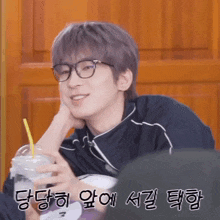 a young man wearing glasses is holding a drink with a straw