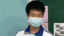 a young man wearing a mask is standing in front of a chalkboard .