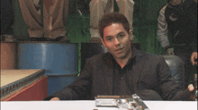 a man in a black suit sits at a table with a gun on it