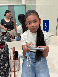 a girl in a white shirt is sitting in a bathroom looking at her phone