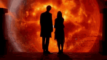 a man and a woman are standing in front of a large fire .