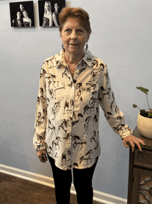 a woman wearing a shirt with horses on it stands in front of a wall of pictures