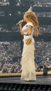 a woman in a white dress is singing into a microphone while standing on a stage in front of a crowd .