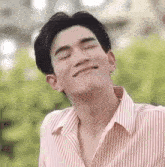 a close up of a young man wearing a striped shirt and smiling with his eyes closed .
