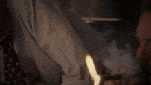 a man in a white shirt and tie smoking a cigar with a fire behind him
