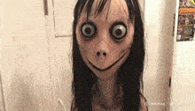 a creepy doll with big eyes and a smiling face is standing in front of a door .