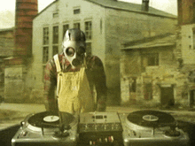 a man wearing overalls and a gas mask is playing records