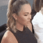 a woman with her hair in a ponytail is wearing earrings and a black tank top