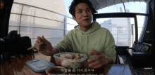 a man in a green hoodie is sitting at a table eating food with chopsticks