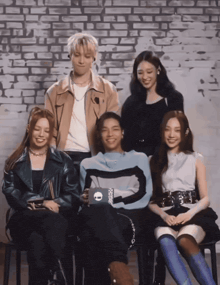 a group of people sitting in front of a brick wall with a man wearing a sweater with the letter o on it