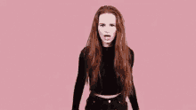 a woman with long red hair is standing in front of a pink background .