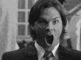 a black and white photo of a man in a suit and tie with his mouth wide open .