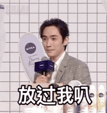 a man in a suit is holding a microphone while standing in front of a nivea sign .