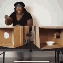 a woman is standing in front of a table with two cardboard boxes and a bowl on it .