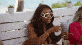 a woman wearing sunglasses is sitting at a table talking to another woman .