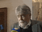 a man with gray hair and a beard is talking into a microphone with the letter l on it