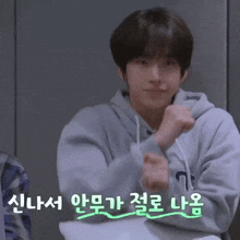 a young man in a grey hoodie is making a funny face with korean writing behind him