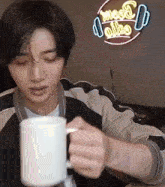 a man is holding a white coffee mug in front of a neon sign that says moo