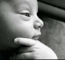 a black and white photo of a baby holding his hand to his chin
