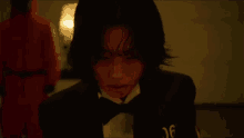 a man in a tuxedo and bow tie with blood on his face is looking at the camera .