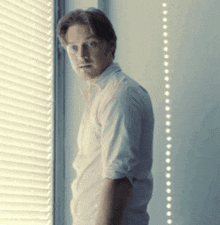 a man in a white shirt is standing in front of a window