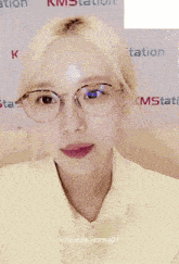 a woman wearing glasses is standing in front of a km station sign