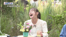 a woman is laughing while sitting at a table with flowers in a vase