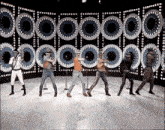 a group of men are dancing on a stage in front of a wall of lights .