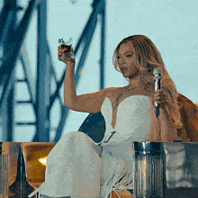 a woman in a white dress holds a microphone and a glass