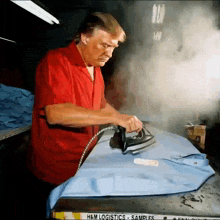 a man in a red shirt is ironing a shirt on a table that says h & m logistics samples