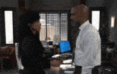 a man and a woman are looking at each other in an office with a laptop that says ' a ' on it