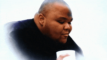 a man with a shaved head is holding a cup of coffee