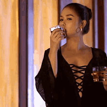 a woman in a black lace up top drinking from a glass