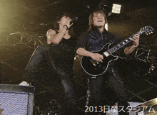 a man singing into a microphone next to a man playing a guitar with the year 2013 on the bottom right